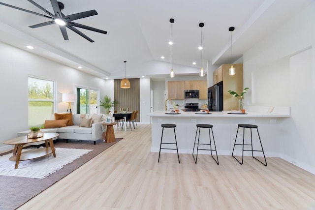 kitchen featuring stainless steel appliances, open floor plan, light countertops, light brown cabinetry, and decorative light fixtures