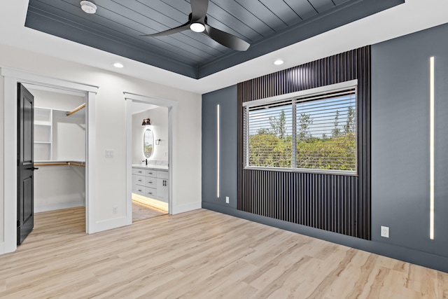 unfurnished bedroom featuring baseboards, wooden ceiling, light wood-style flooring, a spacious closet, and a tray ceiling