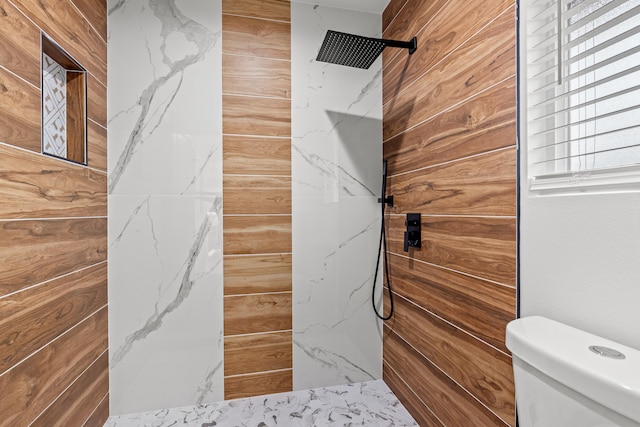 bathroom featuring toilet, wooden walls, and a marble finish shower