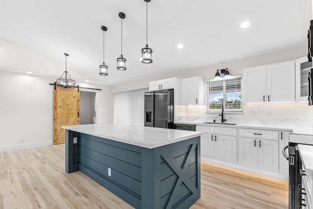 kitchen with a barn door, a kitchen island, stainless steel appliances, white cabinetry, and a sink