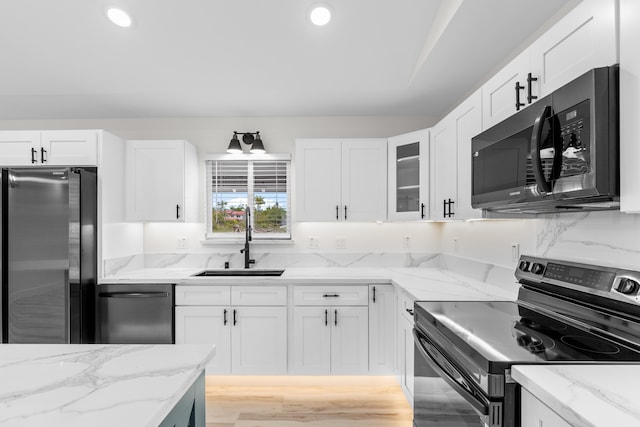 kitchen with white cabinets, light stone counters, glass insert cabinets, stainless steel appliances, and a sink