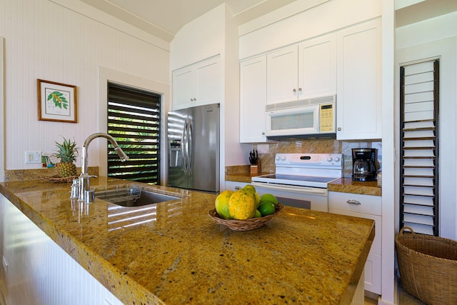 kitchen with stone countertops, white appliances, a sink, white cabinets, and backsplash