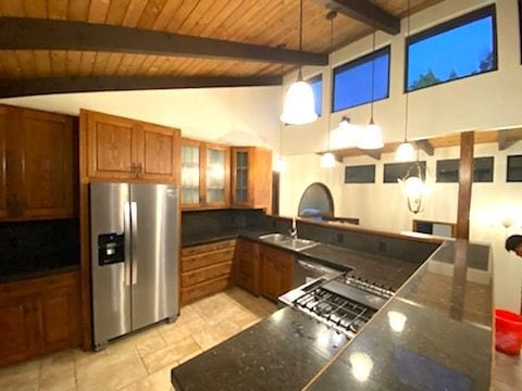 kitchen featuring stainless steel fridge, brown cabinetry, glass insert cabinets, pendant lighting, and a sink