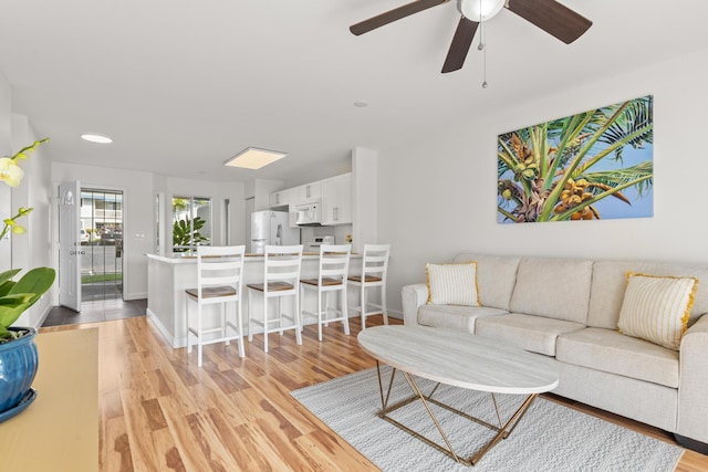 living area with light wood finished floors, ceiling fan, and baseboards