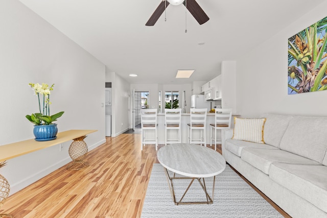 living area with ceiling fan, light wood finished floors, and baseboards