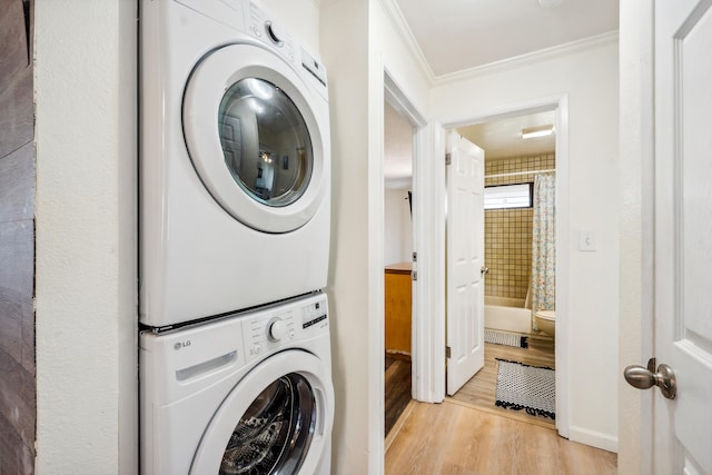 washroom featuring laundry area, baseboards, ornamental molding, light wood-type flooring, and stacked washing maching and dryer