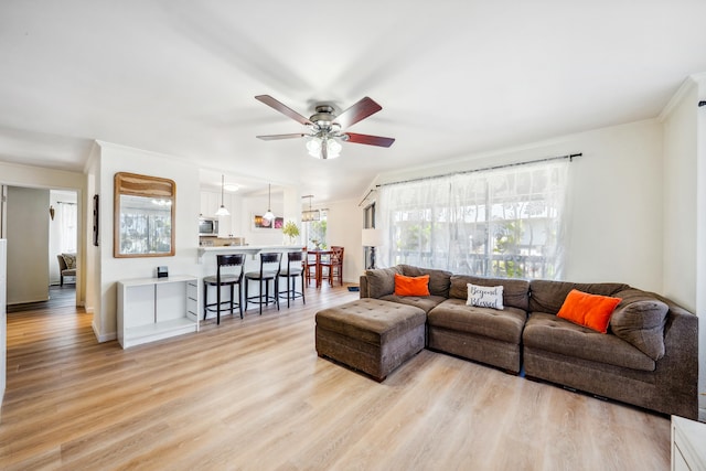 living room with ceiling fan, crown molding, light wood-style flooring, and baseboards