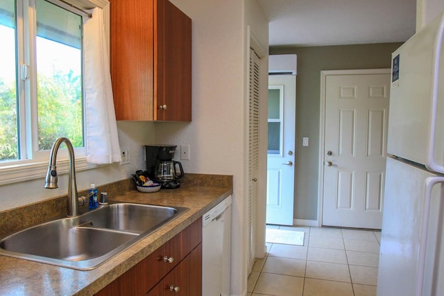 kitchen with dark countertops, brown cabinetry, light tile patterned flooring, a sink, and white appliances