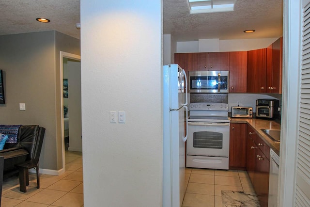 kitchen with dark countertops, white appliances, light tile patterned floors, and a textured ceiling