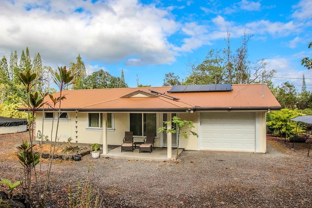 view of front of home featuring a patio, stucco siding, an attached garage, roof mounted solar panels, and driveway