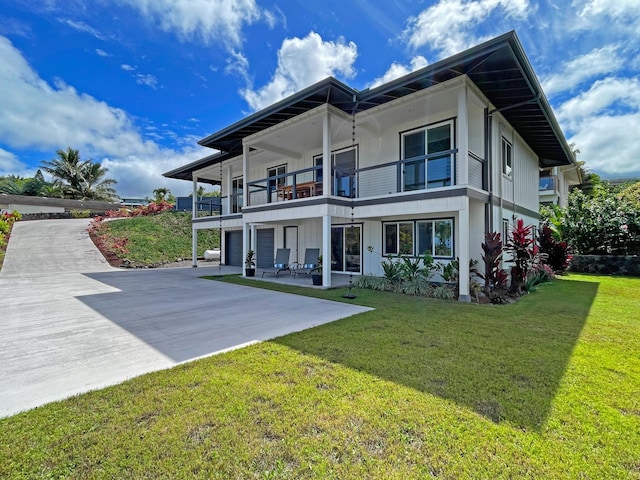 rear view of property featuring a balcony, a garage, driveway, a yard, and a patio area