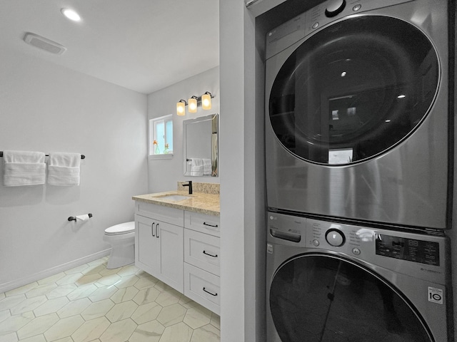 washroom featuring light tile patterned floors, laundry area, a sink, baseboards, and stacked washing maching and dryer