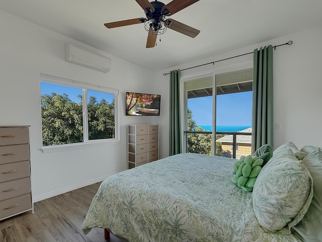 bedroom featuring a wall unit AC, wood finished floors, a ceiling fan, baseboards, and access to outside