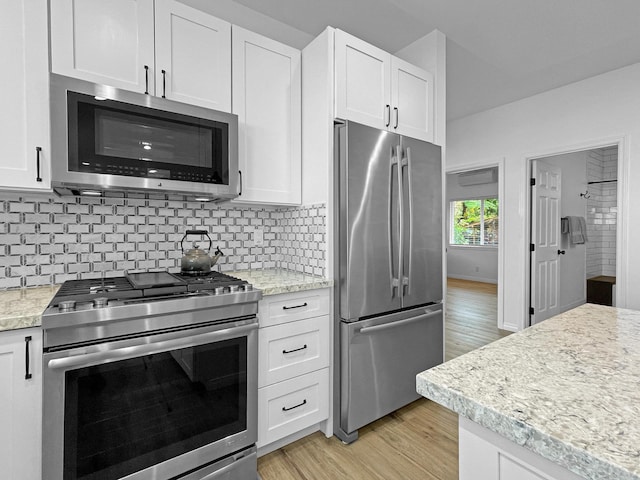 kitchen featuring appliances with stainless steel finishes, white cabinetry, light wood finished floors, and tasteful backsplash