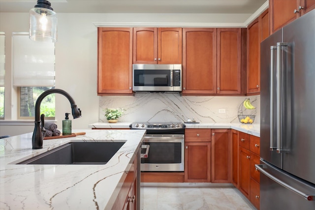 kitchen featuring light stone counters, a sink, hanging light fixtures, appliances with stainless steel finishes, and tasteful backsplash