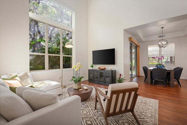 living area with a notable chandelier, wood finished floors, visible vents, baseboards, and a raised ceiling