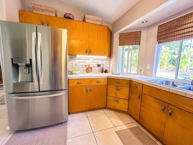 kitchen featuring light tile patterned flooring, brown cabinets, tile counters, and stainless steel fridge with ice dispenser