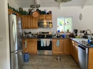 kitchen featuring appliances with stainless steel finishes, brown cabinetry, and beam ceiling