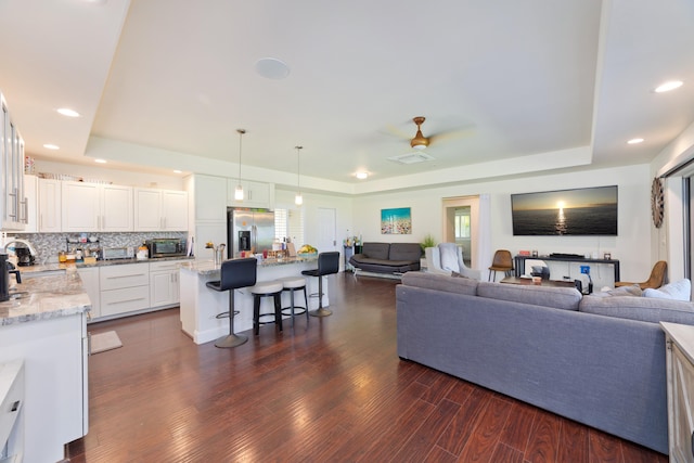 living area featuring dark wood-style floors, a raised ceiling, a ceiling fan, and recessed lighting