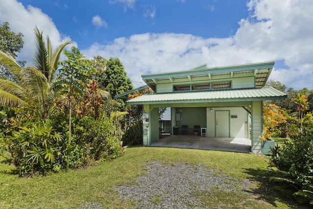 back of property featuring driveway, metal roof, a carport, and a yard