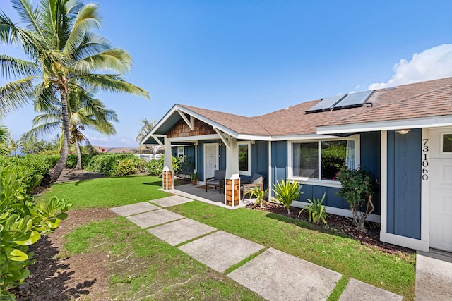 rear view of house with a yard, solar panels, a shingled roof, a porch, and board and batten siding