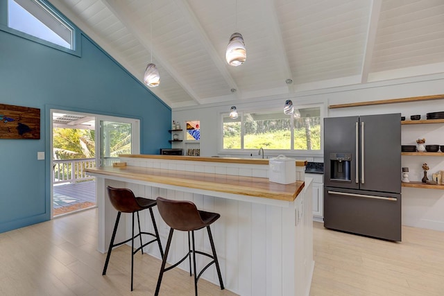 kitchen featuring high end fridge, white cabinets, hanging light fixtures, and a breakfast bar area