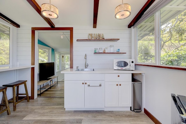 kitchen with white microwave, a sink, white cabinetry, light countertops, and light wood-type flooring