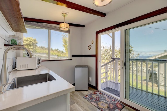 kitchen with light countertops, a sink, beam ceiling, and light wood-style floors