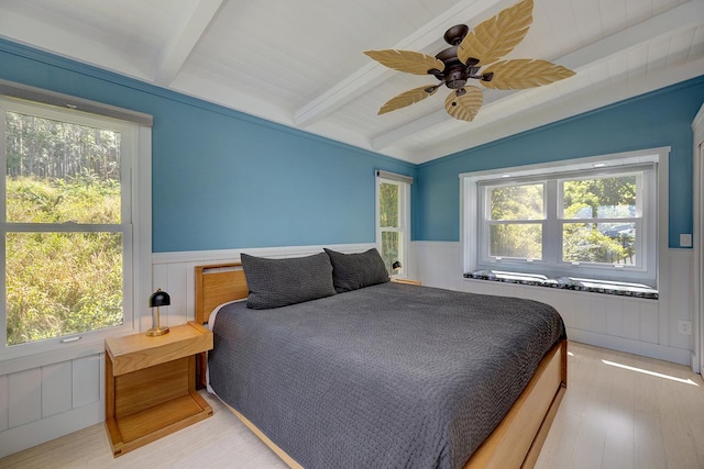 bedroom with vaulted ceiling with beams, multiple windows, and a wainscoted wall