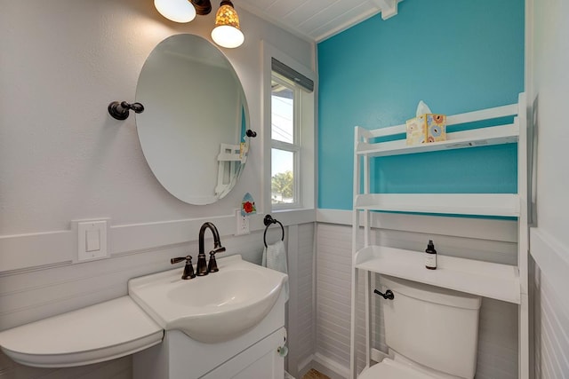 half bathroom with a wainscoted wall, vanity, and toilet