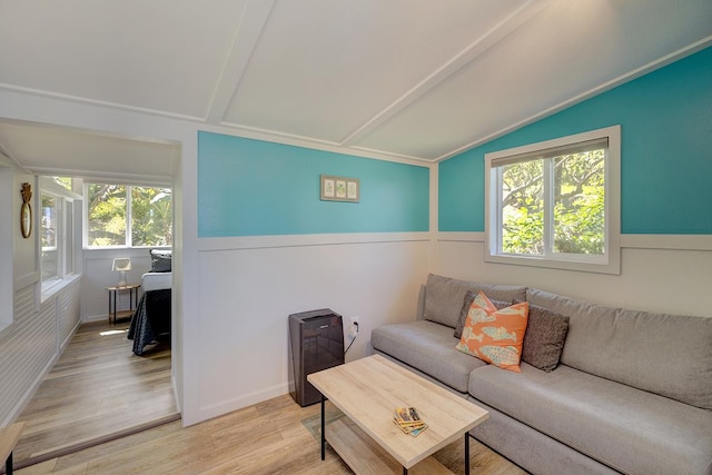 living room featuring lofted ceiling, wainscoting, and light wood-type flooring