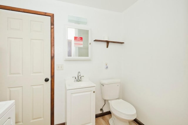 half bathroom with washer / clothes dryer, toilet, vanity, wood finished floors, and baseboards