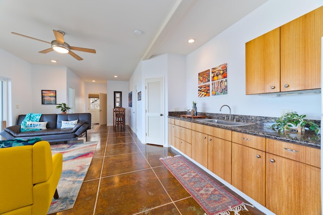 kitchen featuring ceiling fan, recessed lighting, a sink, open floor plan, and dark stone counters