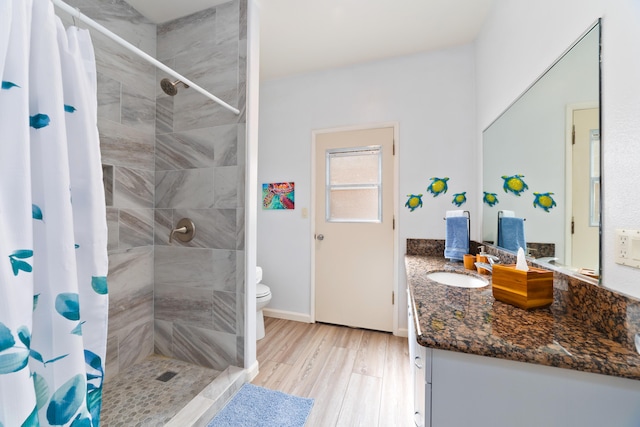 full bath featuring toilet, a tile shower, wood finished floors, and vanity