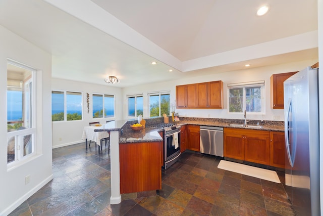 kitchen featuring appliances with stainless steel finishes, brown cabinetry, a sink, and a peninsula