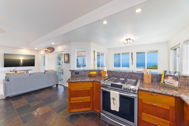 kitchen with recessed lighting, open floor plan, stainless steel gas stove, brown cabinetry, and dark stone countertops