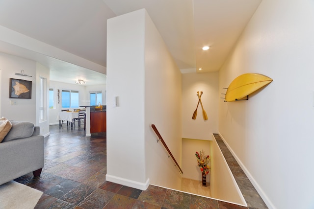 corridor featuring stone tile flooring, baseboards, and an upstairs landing