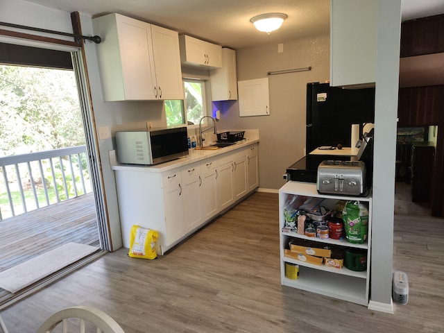 kitchen featuring white cabinetry, stainless steel microwave, a sink, and freestanding refrigerator