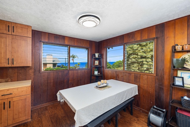 dining space with a textured ceiling, dark wood-type flooring, and wood walls