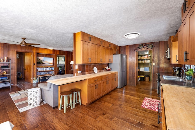 kitchen with appliances with stainless steel finishes, dark wood-type flooring, a sink, and wood walls