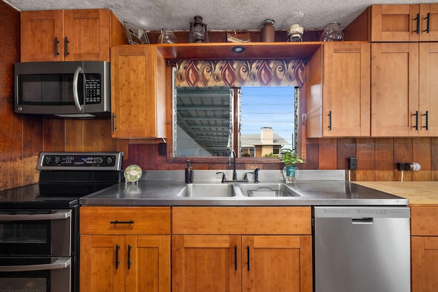 kitchen with a textured ceiling, wood walls, a sink, light countertops, and appliances with stainless steel finishes