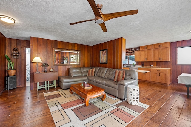 living room featuring a ceiling fan, wooden walls, a textured ceiling, and hardwood / wood-style floors