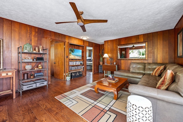 living room featuring wood walls, ceiling fan, a textured ceiling, and wood finished floors