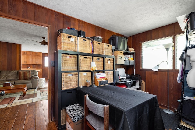 interior space with a textured ceiling, ceiling fan, wooden walls, and hardwood / wood-style floors