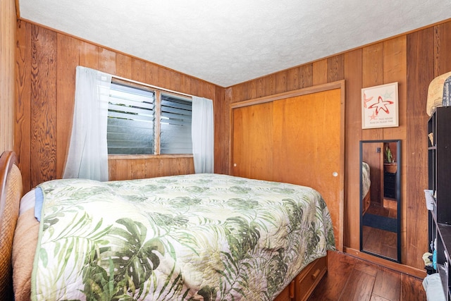 bedroom featuring a closet, wood walls, a textured ceiling, and hardwood / wood-style floors