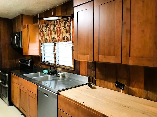 kitchen with brown cabinetry, butcher block countertops, stainless steel appliances, a textured ceiling, and a sink