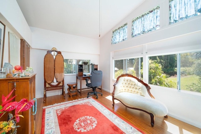 living area with high vaulted ceiling, baseboards, and wood finished floors