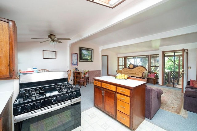 kitchen with light countertops, brown cabinetry, a ceiling fan, open floor plan, and stainless steel gas range oven