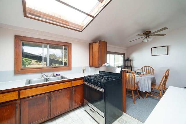 kitchen with range with gas stovetop, brown cabinets, light countertops, lofted ceiling with skylight, and a sink