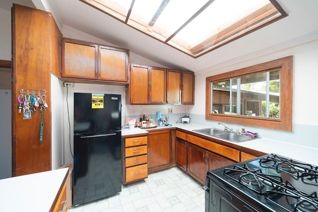 kitchen featuring brown cabinetry, lofted ceiling with skylight, light countertops, black appliances, and a sink